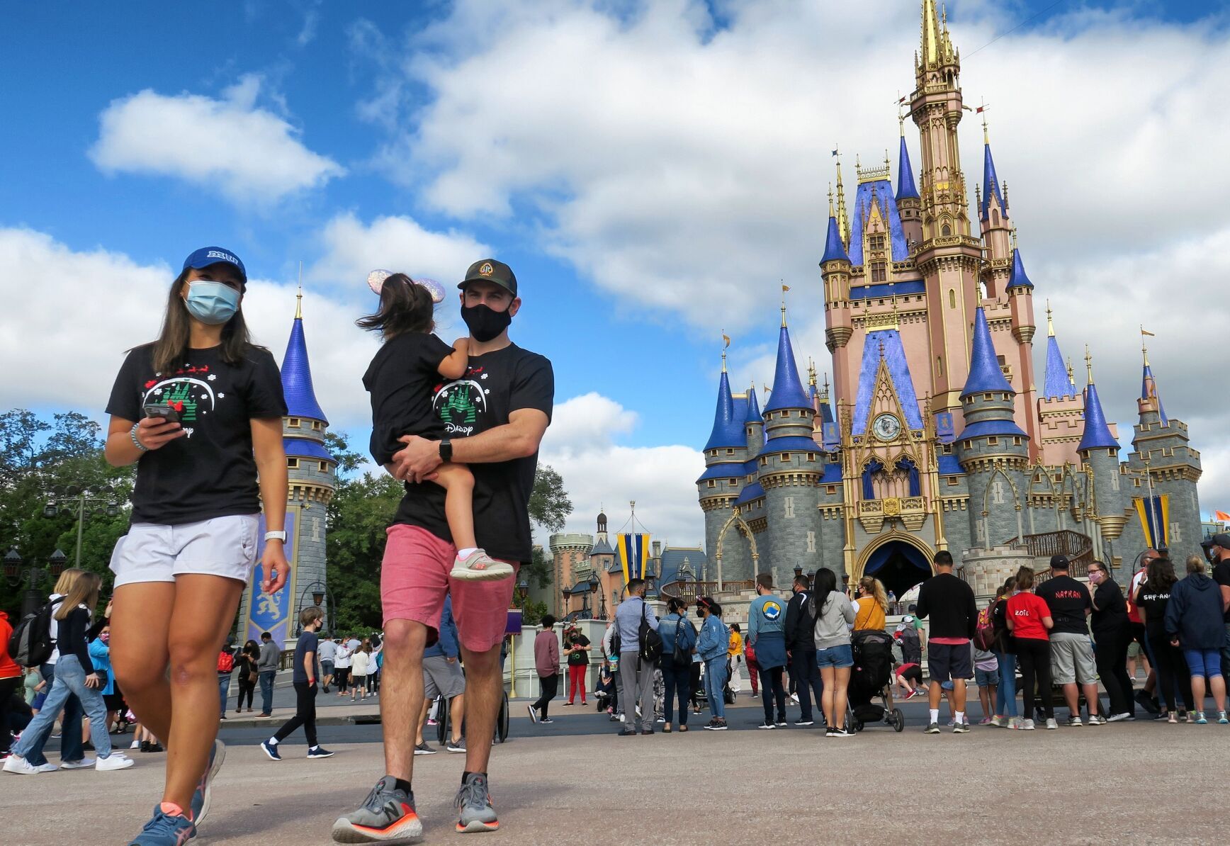 A masked family walks past Cinderella Castle, which was given a new color scheme in 2020..